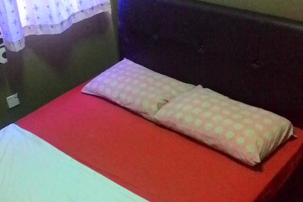 Ein Bett mit roter Matratze und weißer Bettdecke, ein Kopfkissen mit Punkte-Muster und ein dunkles Kopfteil.