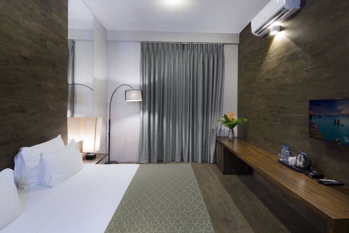 Quarto de hotel com cama, escrivaninha, luminária, televisão e ar condicionado.