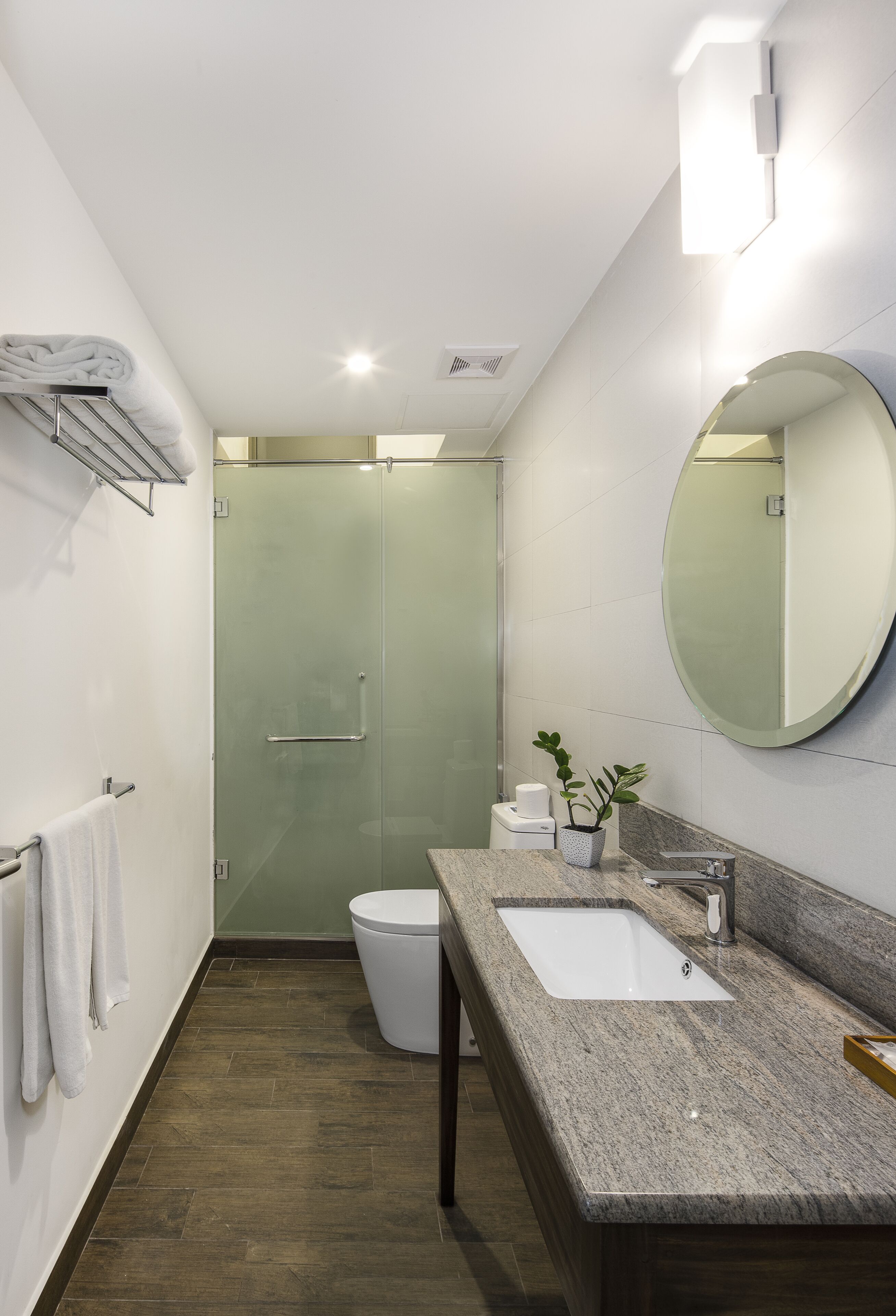 Un baño moderno con cabina de ducha de vidrio, inodoro blanco, lavamanos con encimera de granito y un espejo grande.