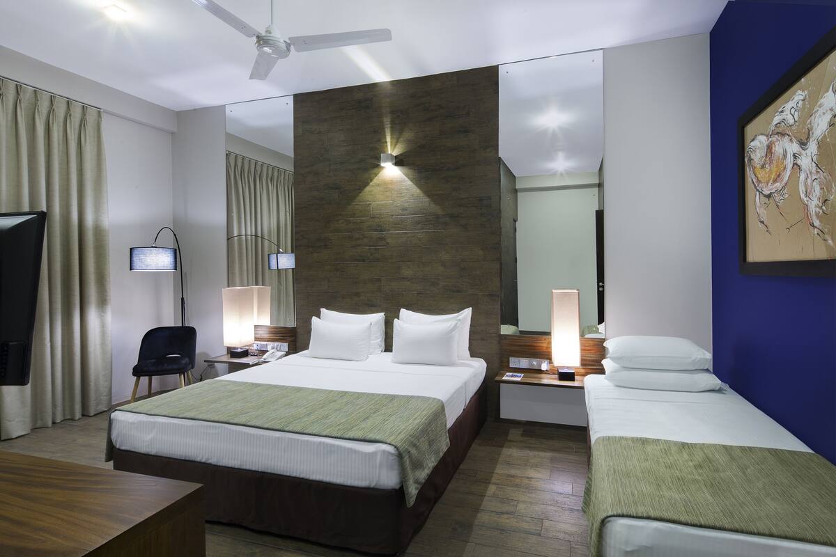 Quarto de hotel com uma cama grande, escrivaninha, cadeira, televisão e ventoinha no teto.