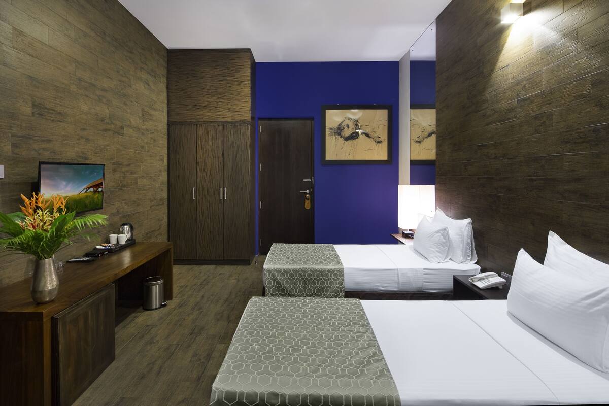 Quarto de hotel com duas camas, uma escrivaninha, televisão e um quadro na parede.