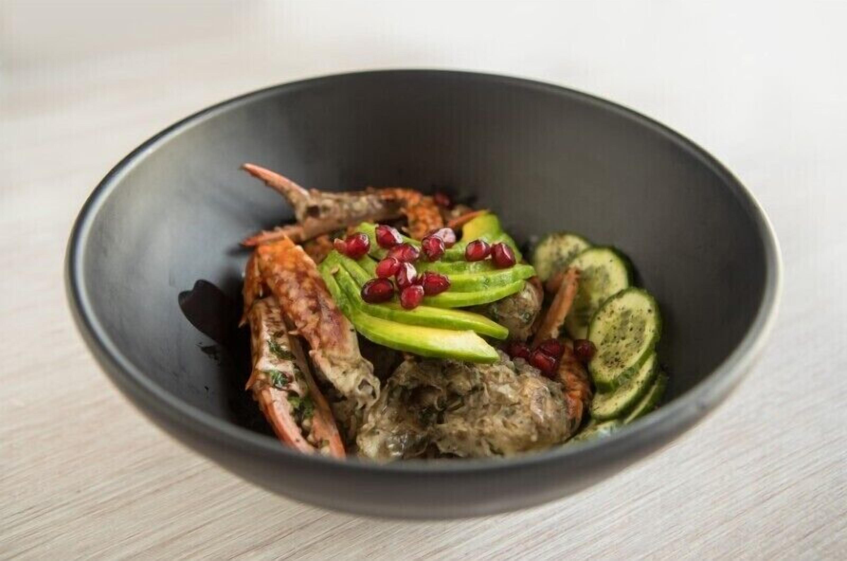 A bowl of food with grilled meat, avocado slices, cucumber slices, and pomegranate seeds.