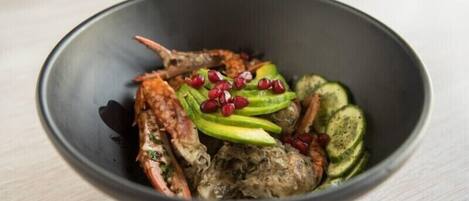 A bowl of food with grilled meat, avocado slices, cucumber slices, and pomegranate seeds.
