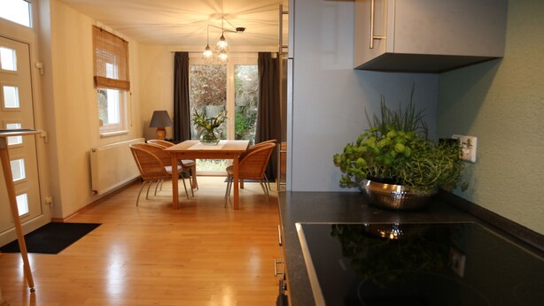 A modern kitchen with a black stove, wooden flooring, a dining table with chairs, and a potted plant on the counter.