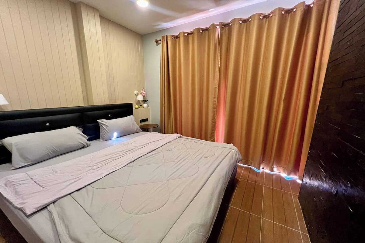 A hotel room with a bed, curtains, a nightstand, and a wall with a textured pattern.