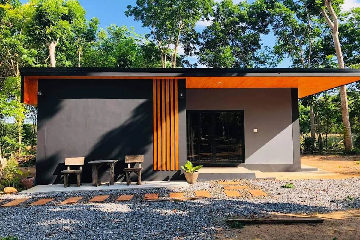 A modern building with a black exterior, wooden slats, and a gravel pathway leading to a bench and table.
