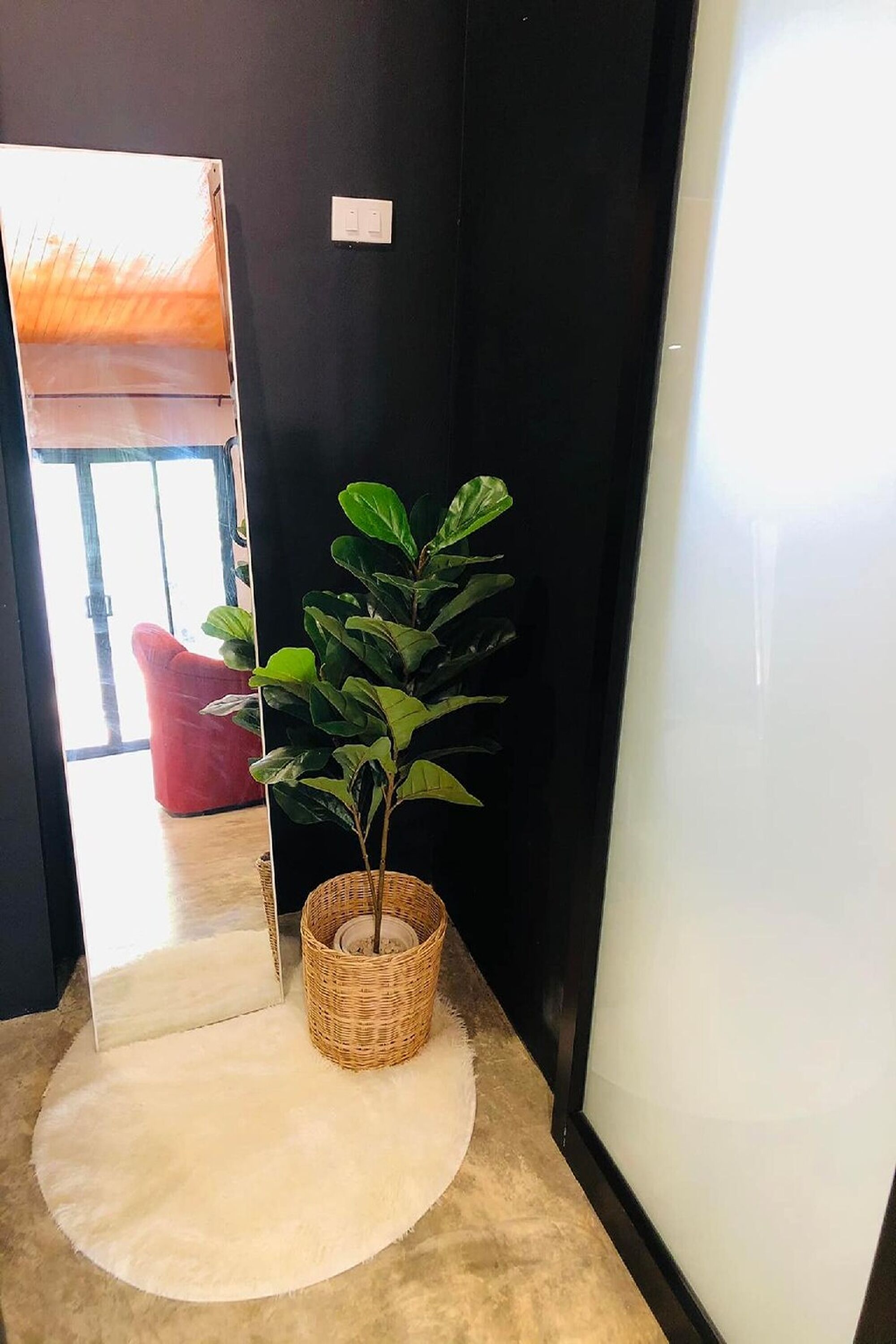 Un pasillo con un espejo grande, una cesta de mimbre con una planta y una silla roja al fondo.