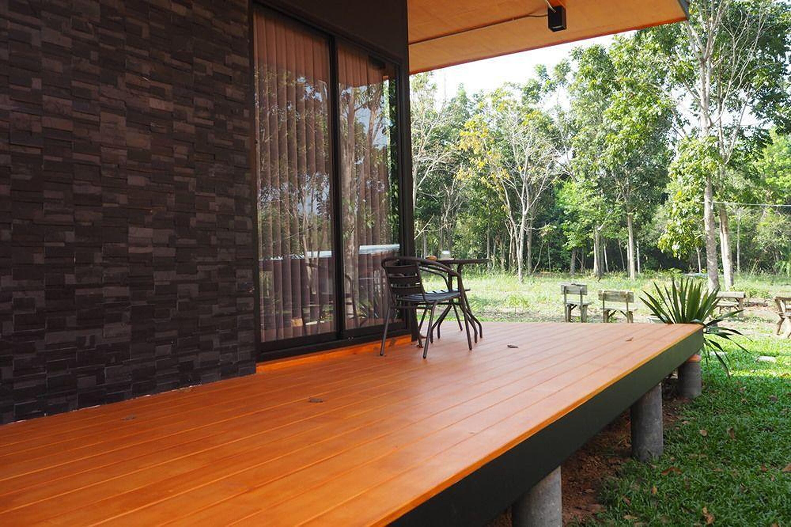 Une terrasse en bois avec un banc et des chaises, un mur en briques et une vue sur un jardin avec des arbres et une table de pique-nique.