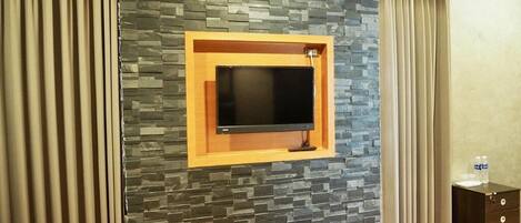 Una habitación con pared de piedra, televisor montado y mueble de madera con cajones.