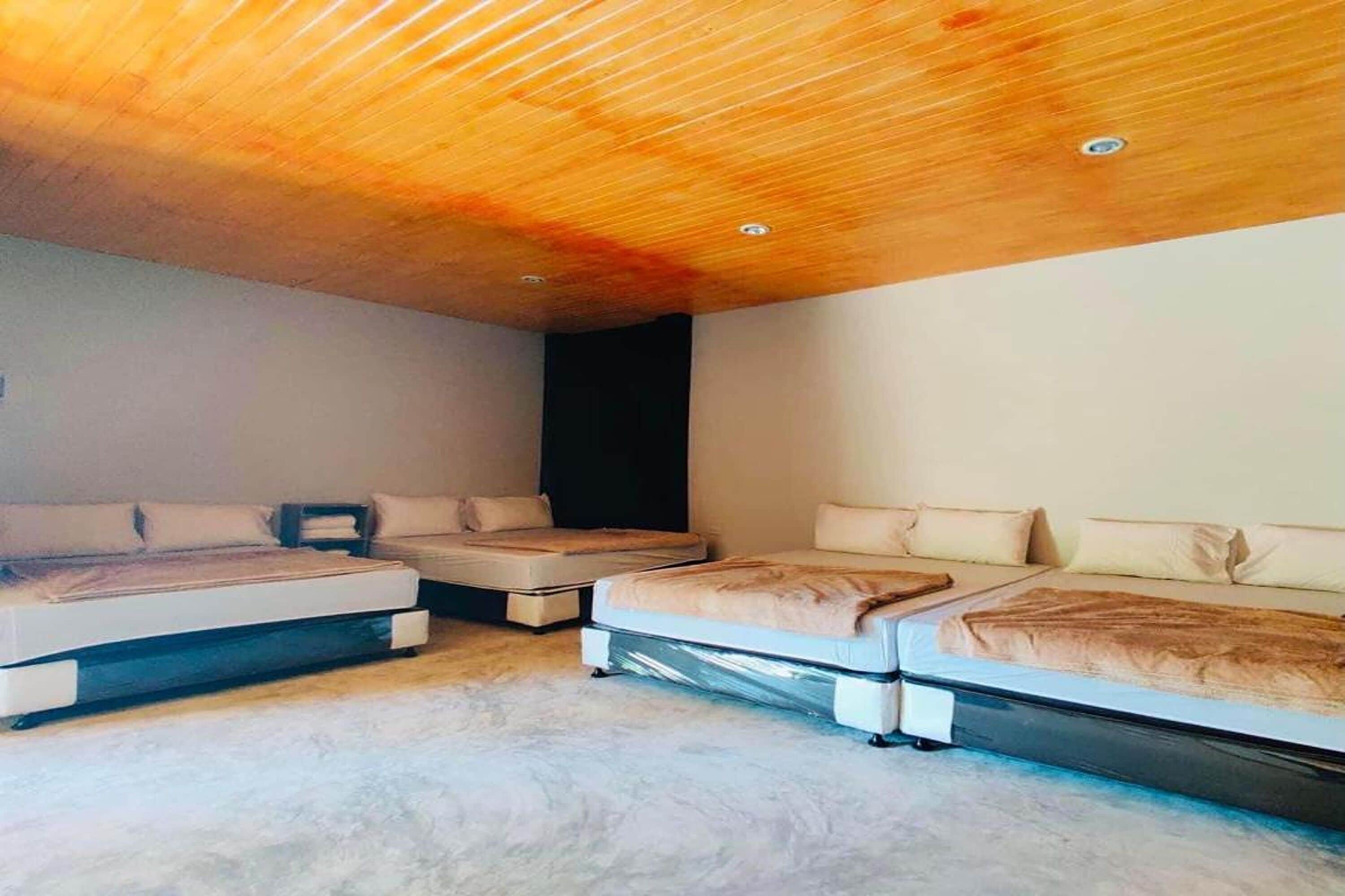 Un dormitorio con tres camas dispuestas en fila, techo de madera y suelo de color claro.