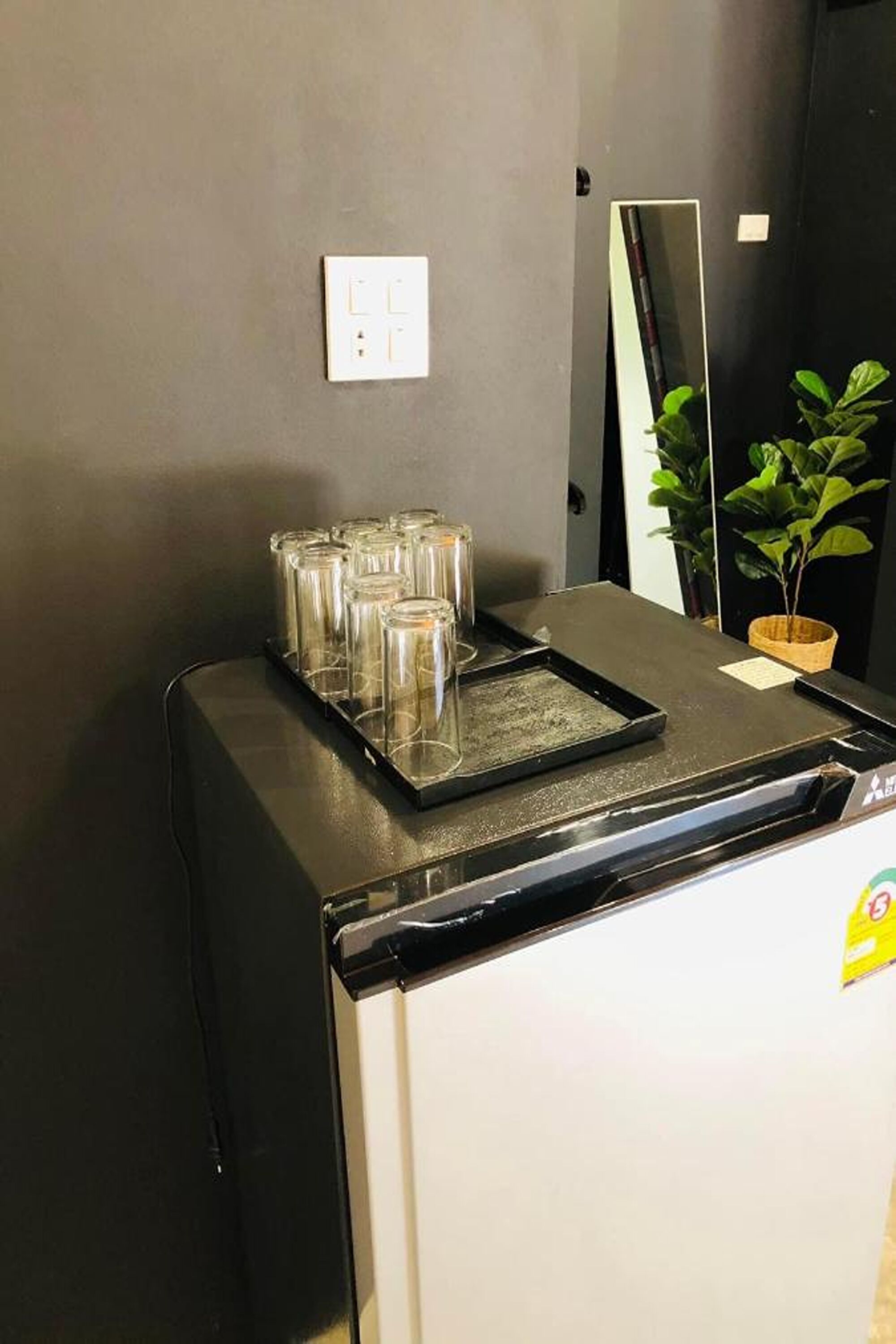 Un coin cuisine comprenant un réfrigérateur, une pile de verres, une plante en pot et un miroir accroché au mur.