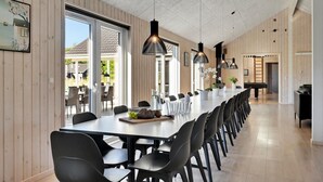 Una larga mesa de comedor con sillas negras, un piano y vistas al exterior.