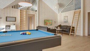 Una mesa de billar con bolas, un sofá, un televisor y una escalera en una habitación con paredes de madera y un techo alto.
