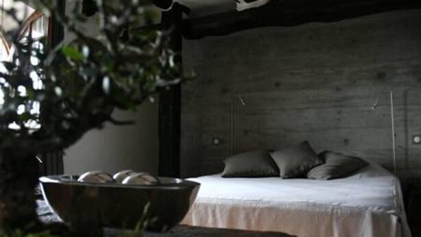 Quarto com cabeceira de madeira, cama com roupa de cama branca e um vaso sobre uma mesa.