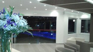 En moderne hotellobby med reception, behagelige siddepladser og udsigt til et poolområde.