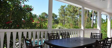 A covered patio with a round table and six chairs, surrounded by a white railing.