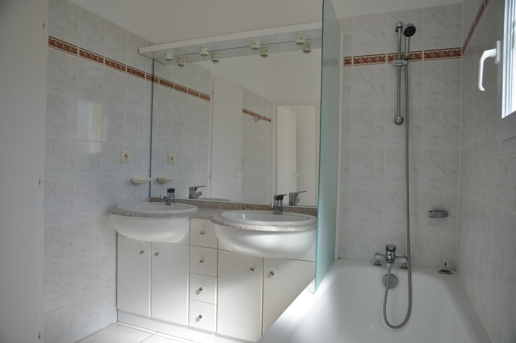 A modern bathroom with two sinks, a large mirror, and a walk-in shower.