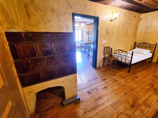 A room with a wooden floor, a bed, a chair, and a fireplace with decorative tiles.