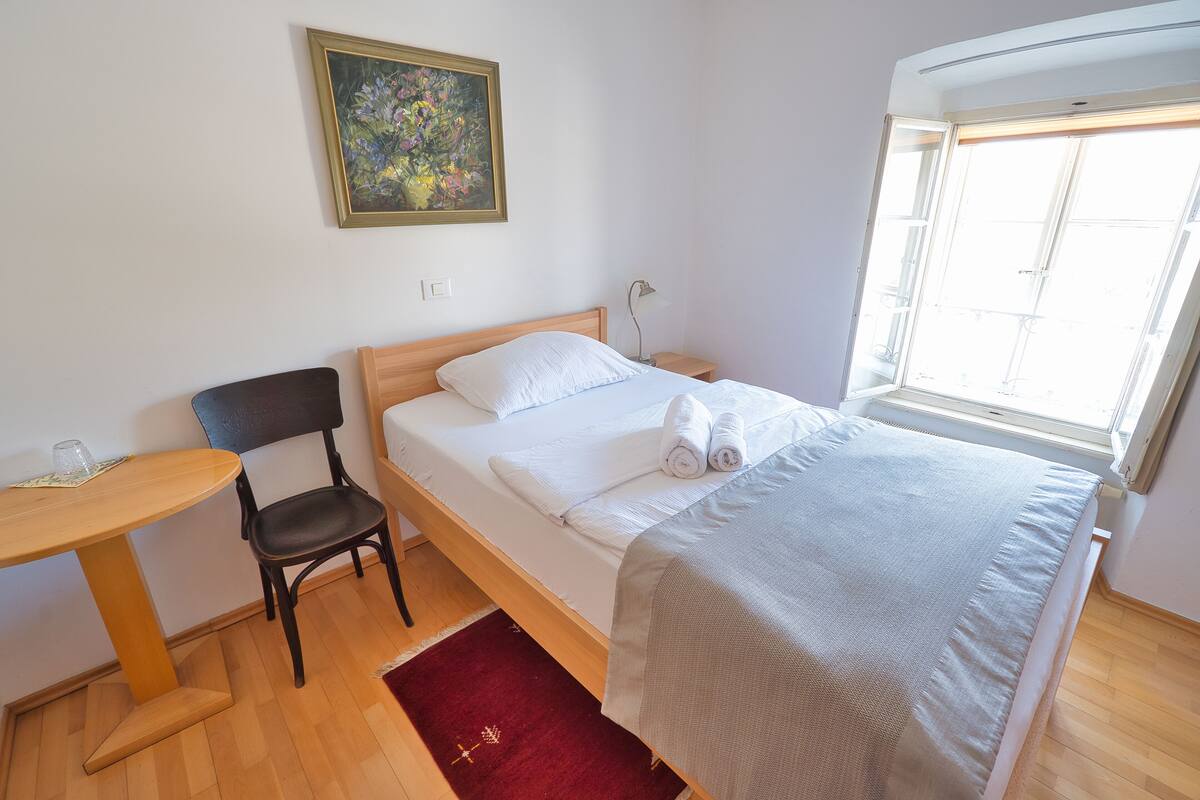 Een keurig opgemaakt slaapkamer met een bed, een stoel, een klein tafeltje en een raam.