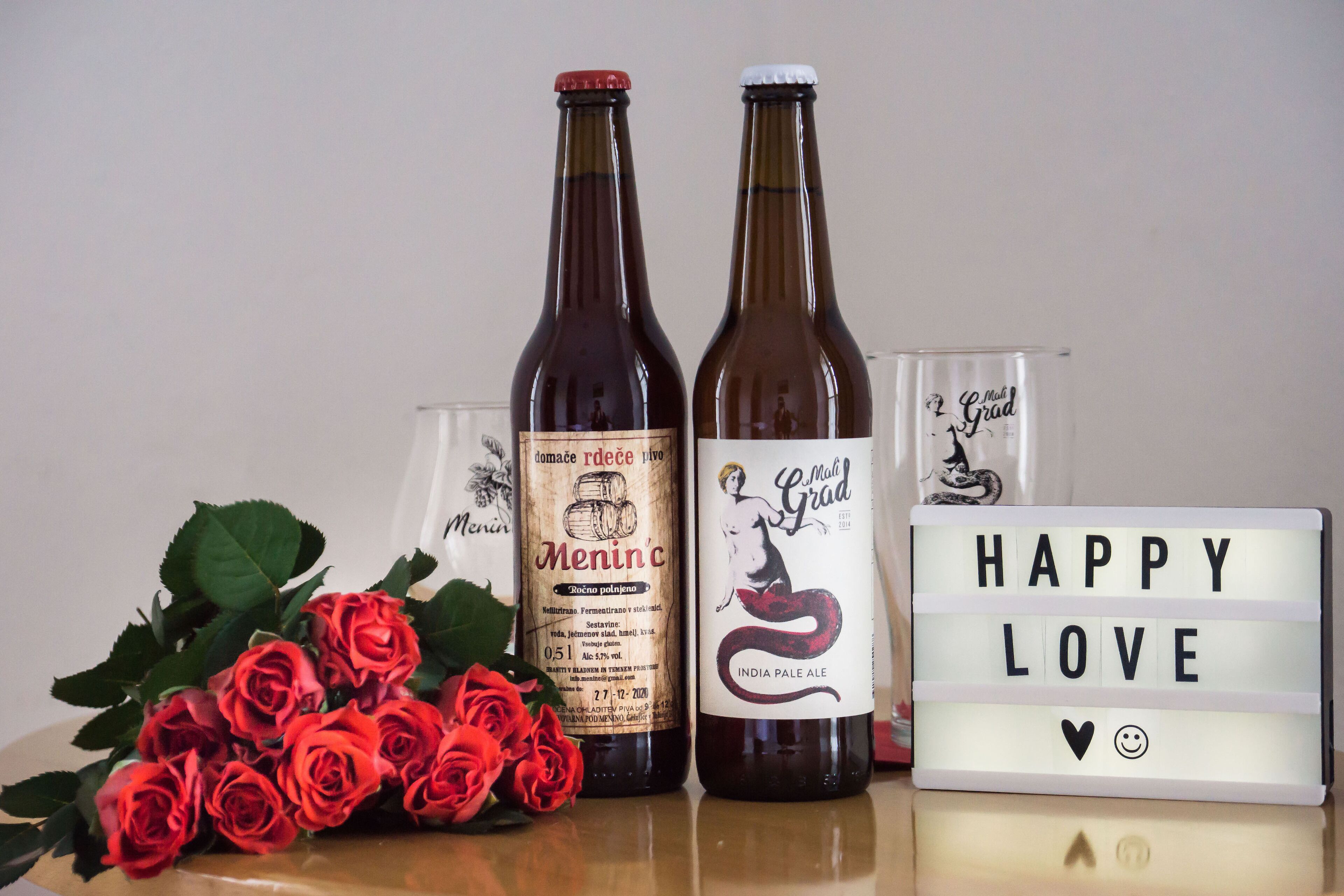Dos botellas de cerveza, un ramo de rosas rojas y una caja de luz con la inscripción 'HAPPY LOVE'.