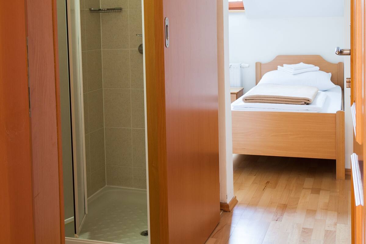 Een kamer met houten vloer, een bed met wit beddengoed en een douchecabine van glas.