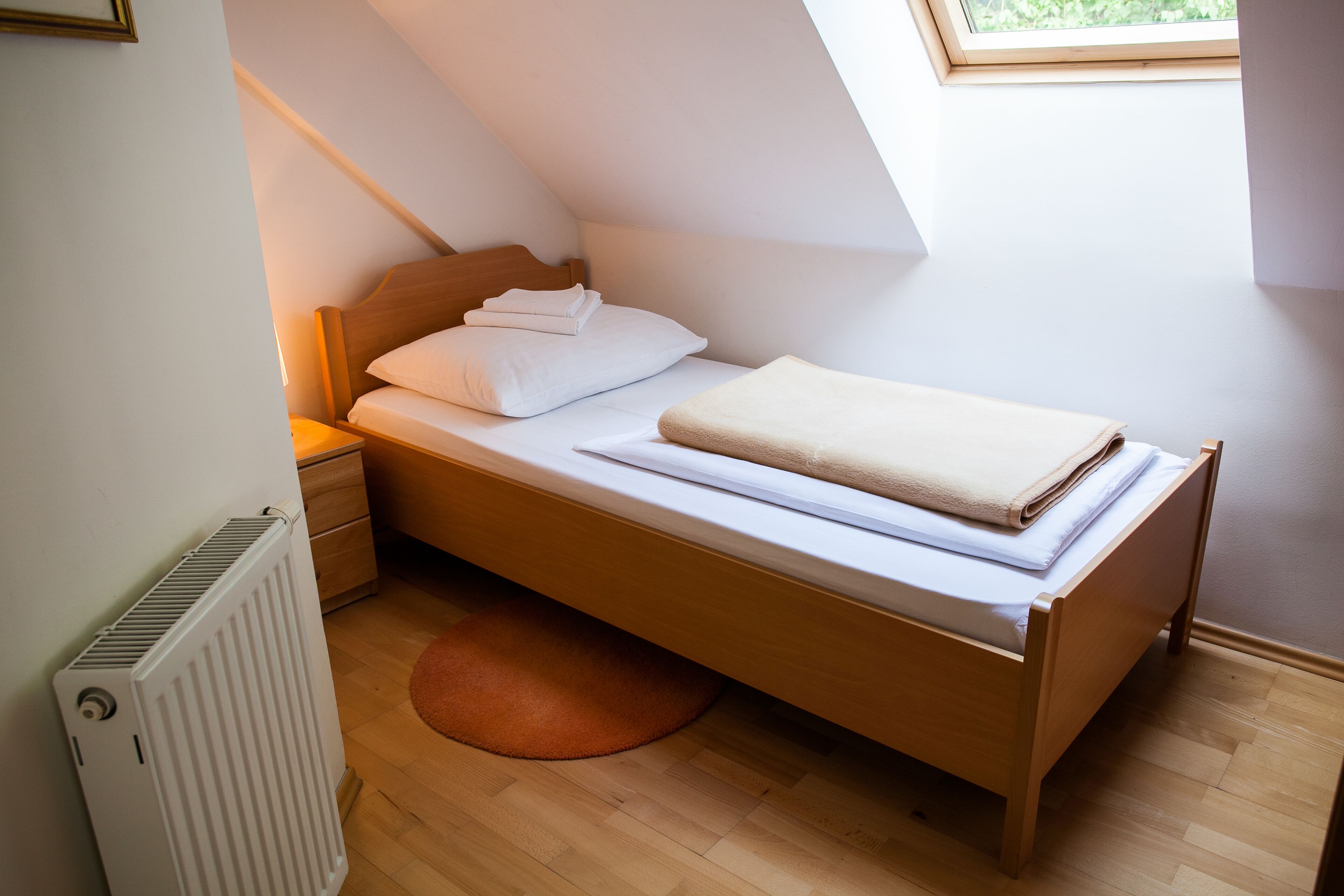 A small, neatly made bed in a room with a sloped ceiling and a window.
