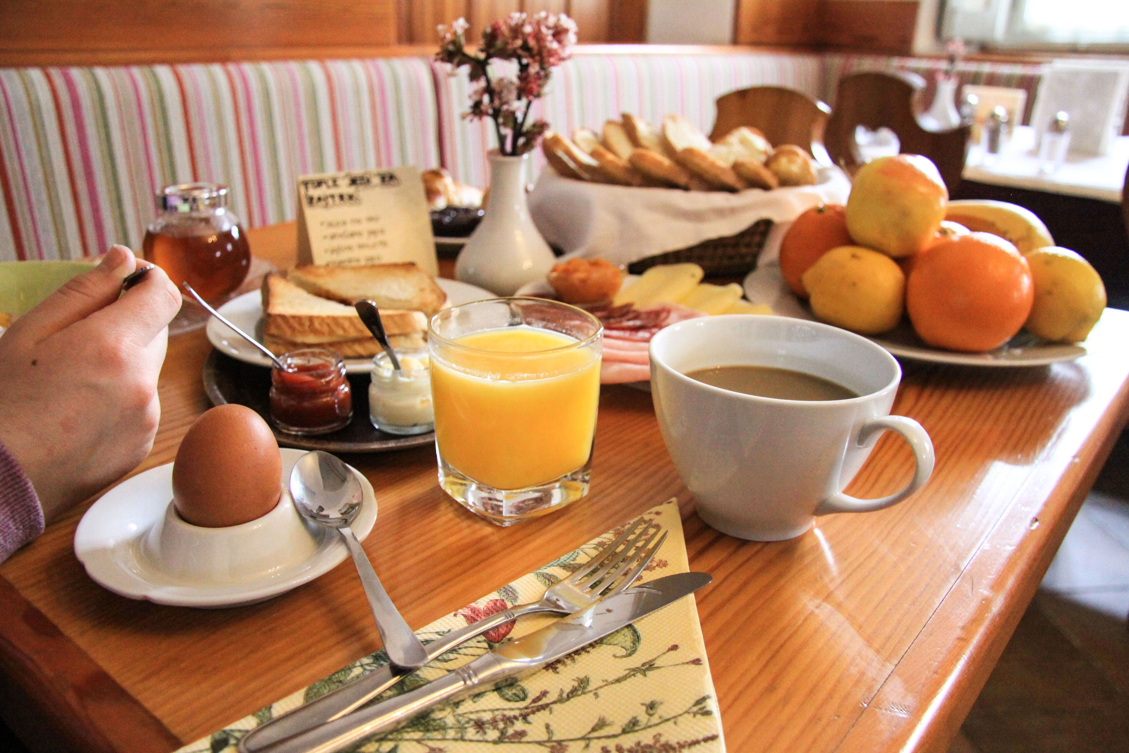 Une table de petit-déjeuner avec des toasts, des œufs, du jus d’orange, du café et un panier de pain.