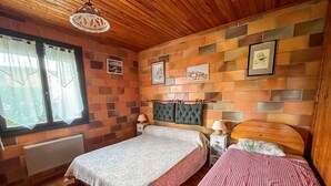 Une chambre avec deux lits, un plancher en bois, des murs décorés d’un motif en briques et une fenêtre avec des rideaux.