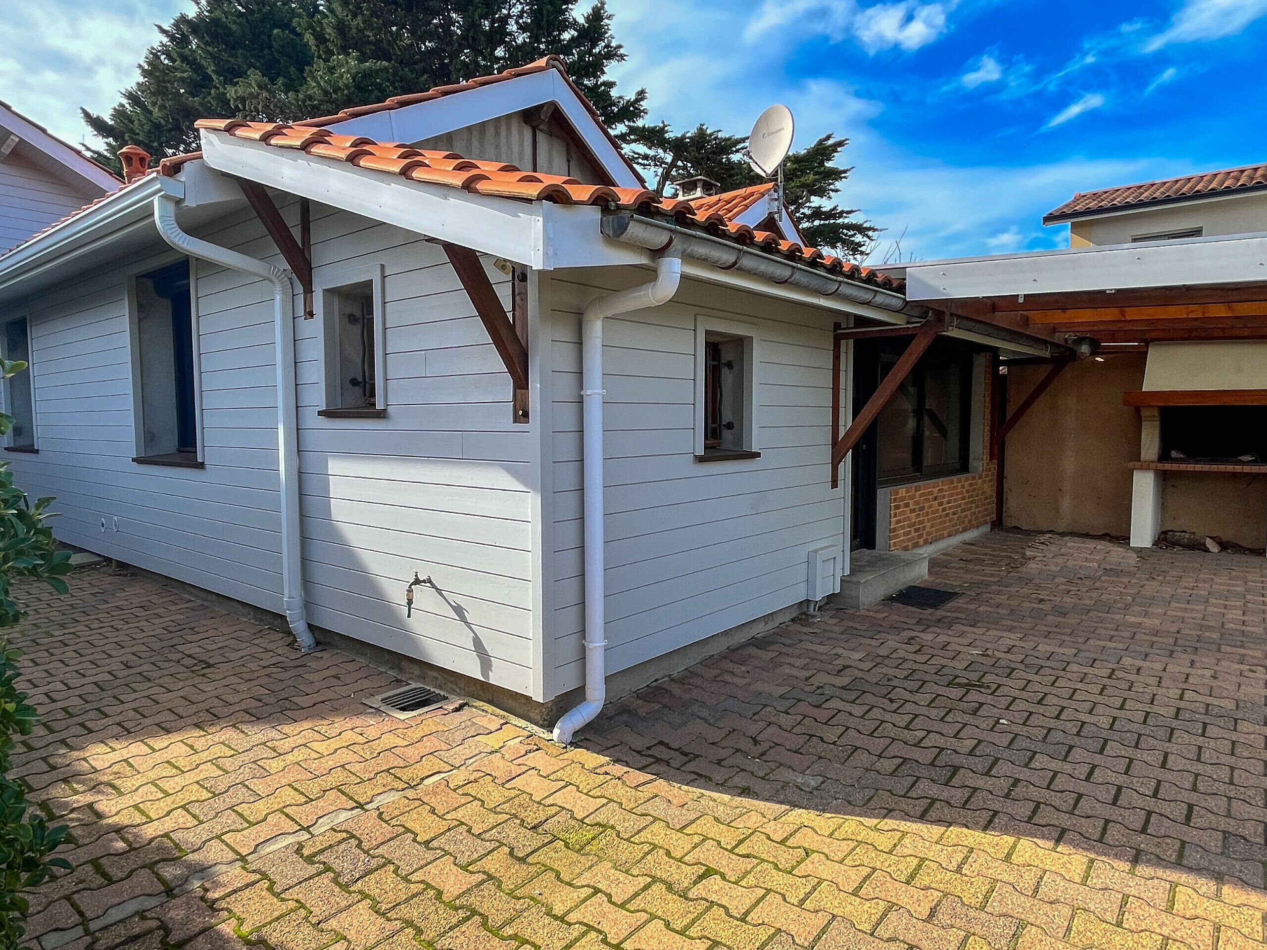 Ein eingeschossiges Haus mit Ziegeldach, Satellitenschüssel und Pflasterterrasse.