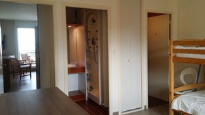 A room with a wooden bunk bed, a bathroom with a shower, and a dining area with chairs and a table.