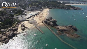 An aerial view of a coastal town with a beach, rocky shoreline, and a pier.