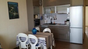 A compact kitchen with a refrigerator, stove, and various utensils hanging on the wall. There is a dining table with chairs and a vase on it.