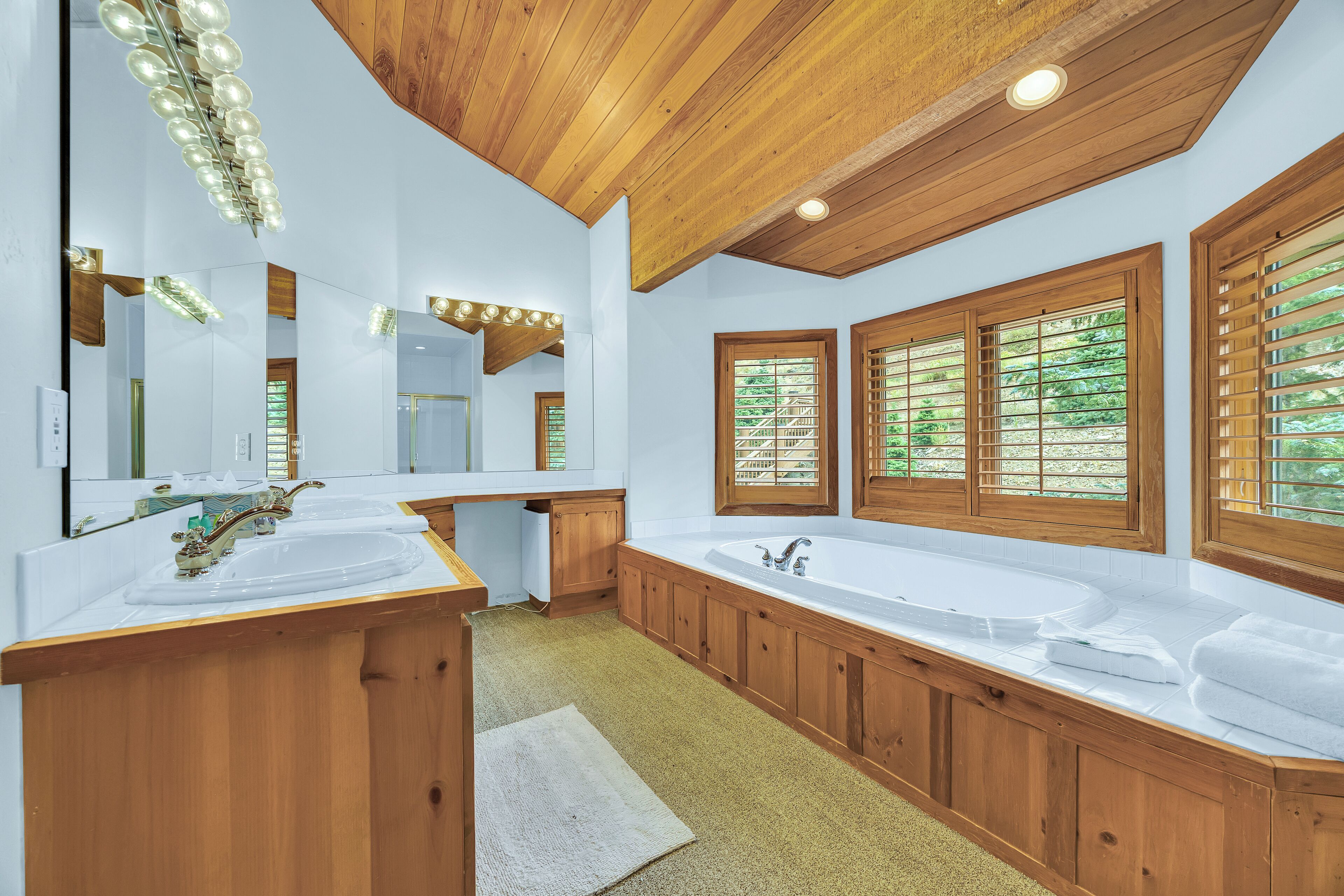 Un baño moderno con dos lavamanos, armarios de madera y ventanas amplias.