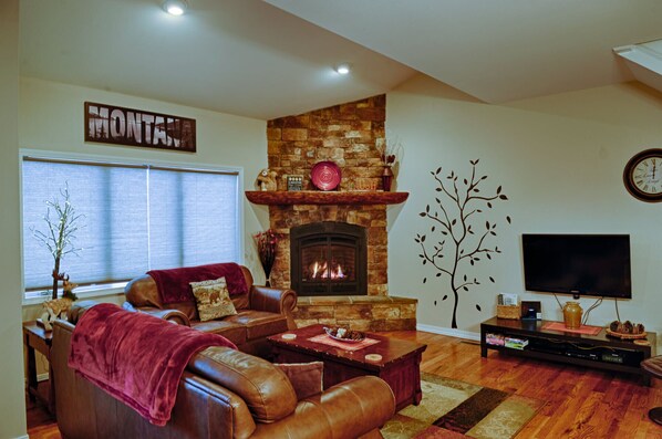 A cozy living room with a stone fireplace, leather sofa, and a flat-screen TV.