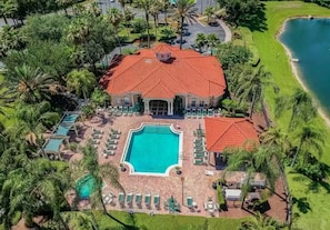 Vista aérea de um resort com piscina central, várias áreas de estar e um edifício grande com telhado de telhas vermelhas.