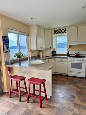 A kitchen with a large island, two red stools, a stove, and a view of the water.