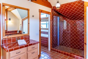 A bathroom with a wooden vanity, a mirror, and a shower area with red tiles.