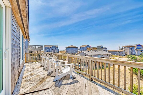 A wooden deck with white chairs, overlooking a row of houses with a clear blue sky.