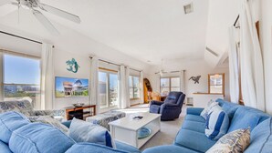 Ein geräumiges Wohnzimmer mit einer großen blauen Sofagarnitur, einem weißen Couchtisch und einem Deckenventilator.