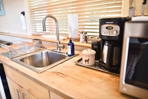 Uma cozinha com uma pia de aço inoxidável, uma cafeteira e um micro-ondas.