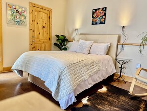 Ein Schlafzimmer mit Bett, Kissen, einem Nachttisch, einer Wandlampe und einem Bild.