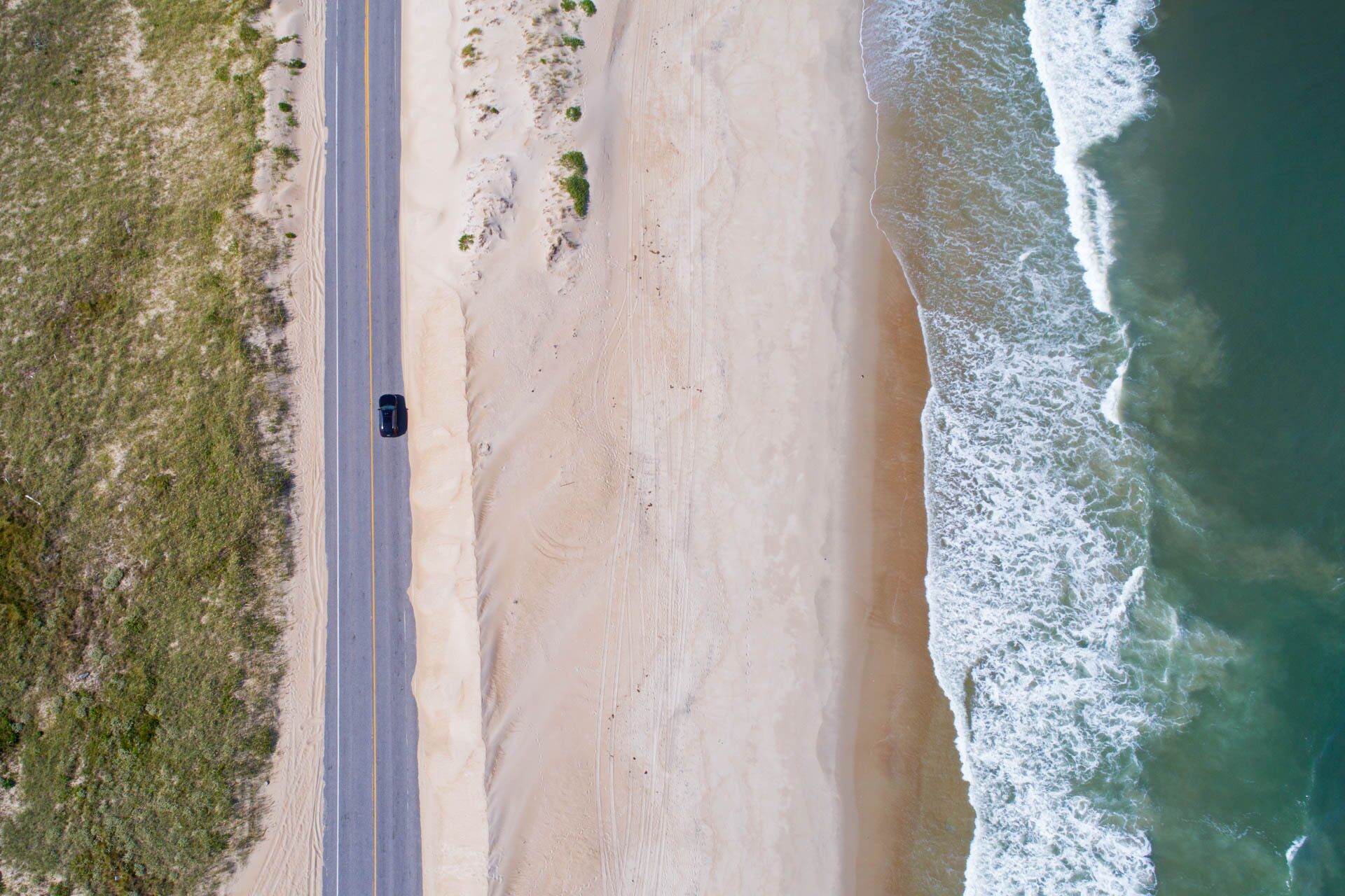 An aerial view of a beach with a road running parallel to the shore.