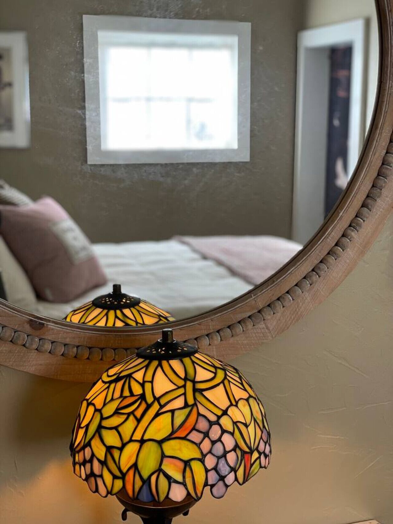 A bedroom with a bed, a bedside table with a lamp, and a mirror on the wall.