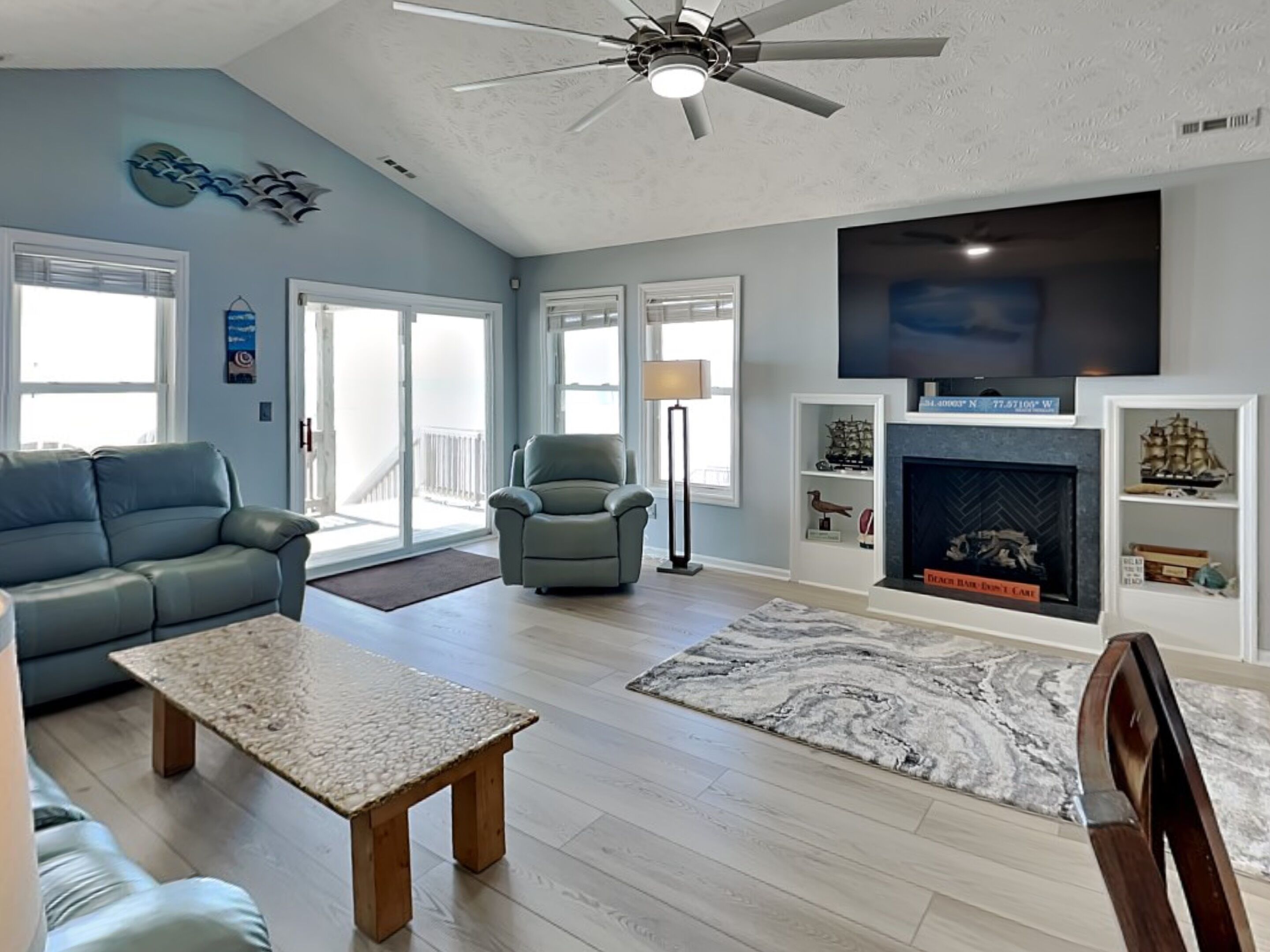 A living room with a sofa, armchair, coffee table, fireplace, TV, and a ceiling fan.