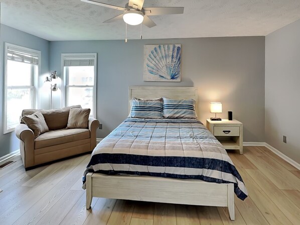 A bedroom with a bed, a nightstand, a ceiling fan, a window, and a couch. - Beach Therapy | Oceanfront, Pet Friendly! (Surf City)