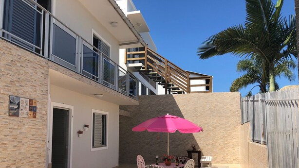 A patio with a table and chairs, a pink umbrella, and a staircase leading to an upper level. - Residencial Dois Amores 2 (Florianópolis)