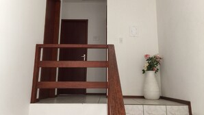 A staircase with a wooden handrail leading to a room with a white door and a potted plant with pink flowers. - Residencial Dois Amores 2 (Florianópolis)