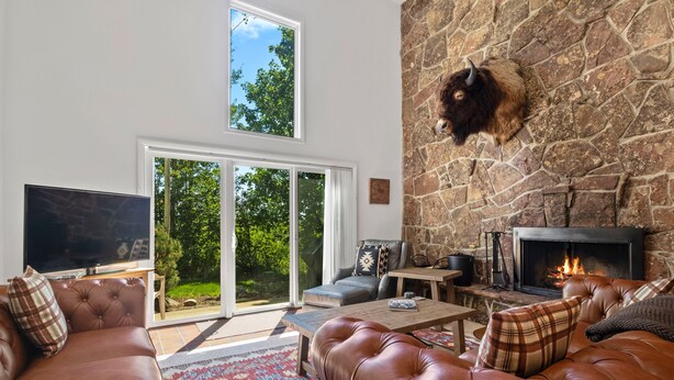 A spacious living room with leather sofas, a stone fireplace, a flat-screen TV, and a large sliding glass door leading to a garden. - RMR: Four Seasons II Unit 1 Condo in Teton Village (Teton Village)