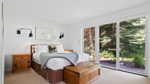 A bedroom with a bed, wooden nightstands, a bedside table, a large window with a view of trees, and a framed picture on the wall. - RMR: Four Seasons II Unit 1 Condo in Teton Village (Teton Village)