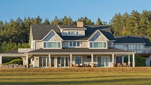 A large, two-story house with a covered porch, stone foundation, and a view of a forested area.